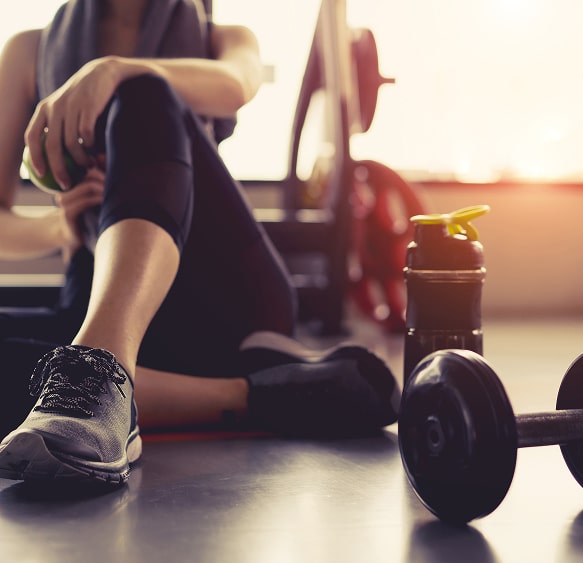 Fitness et Récupération : Repos au gym avec haltère. Athlète s'étirant et se reposant sur le sol du gym. Gros plan sur la chaussure de sport, l'haltère et la bouteille de récupération.