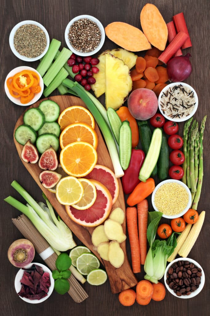 Alimentation saine: variété de fruits, légumes et superaliments frais. Fruits frais (agrumes, figues), légumes colorés (carottes, asperges, poivrons), graines, céréales et épices sur une planche de bois rustique.