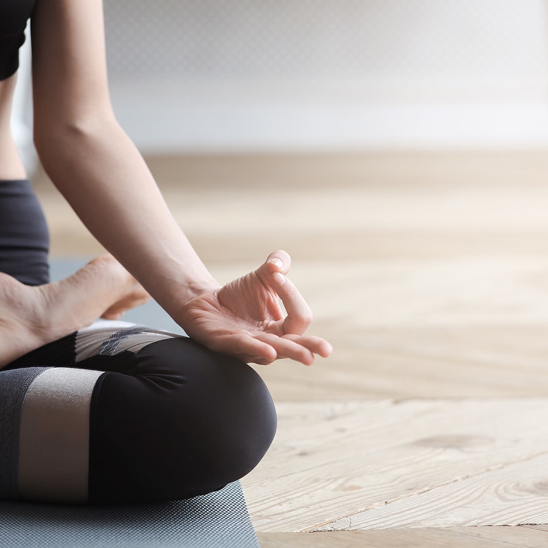 Méditation : Calme et concentration avec le Gyan Mudra. Personne en méditation, assise en tailleur sur un tapis. La main droite forme le Gyan Mudra sur le genou, dans une salle lumineuse.